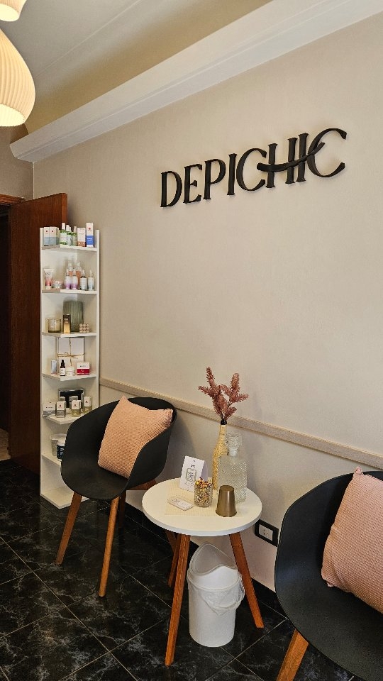 La sala de espera de Depichic: el cartel en la pared, un estante con productos y dos sillas con almohadones